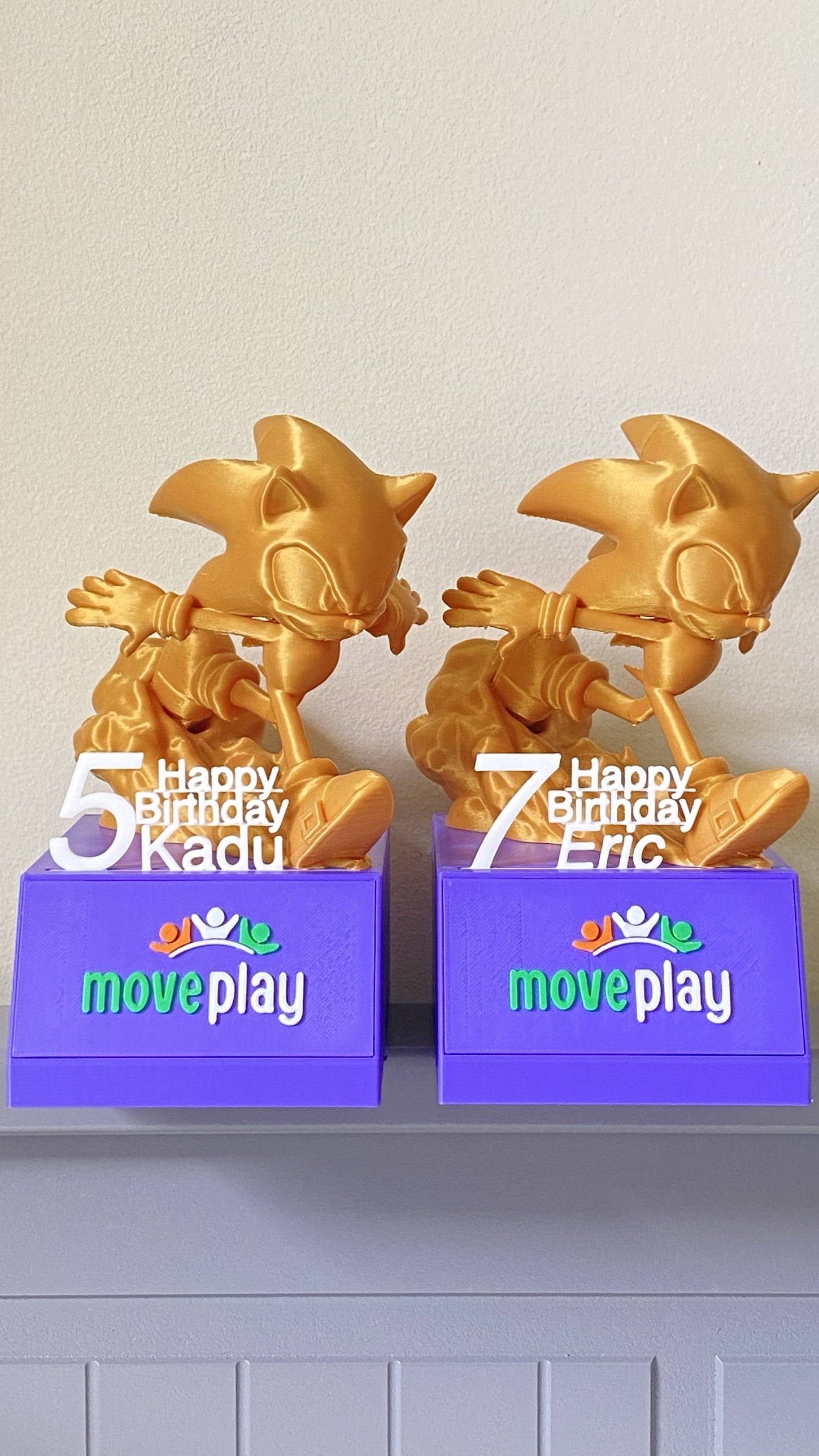 Two gold character trophies with birthday names, on MovePlay branded bases